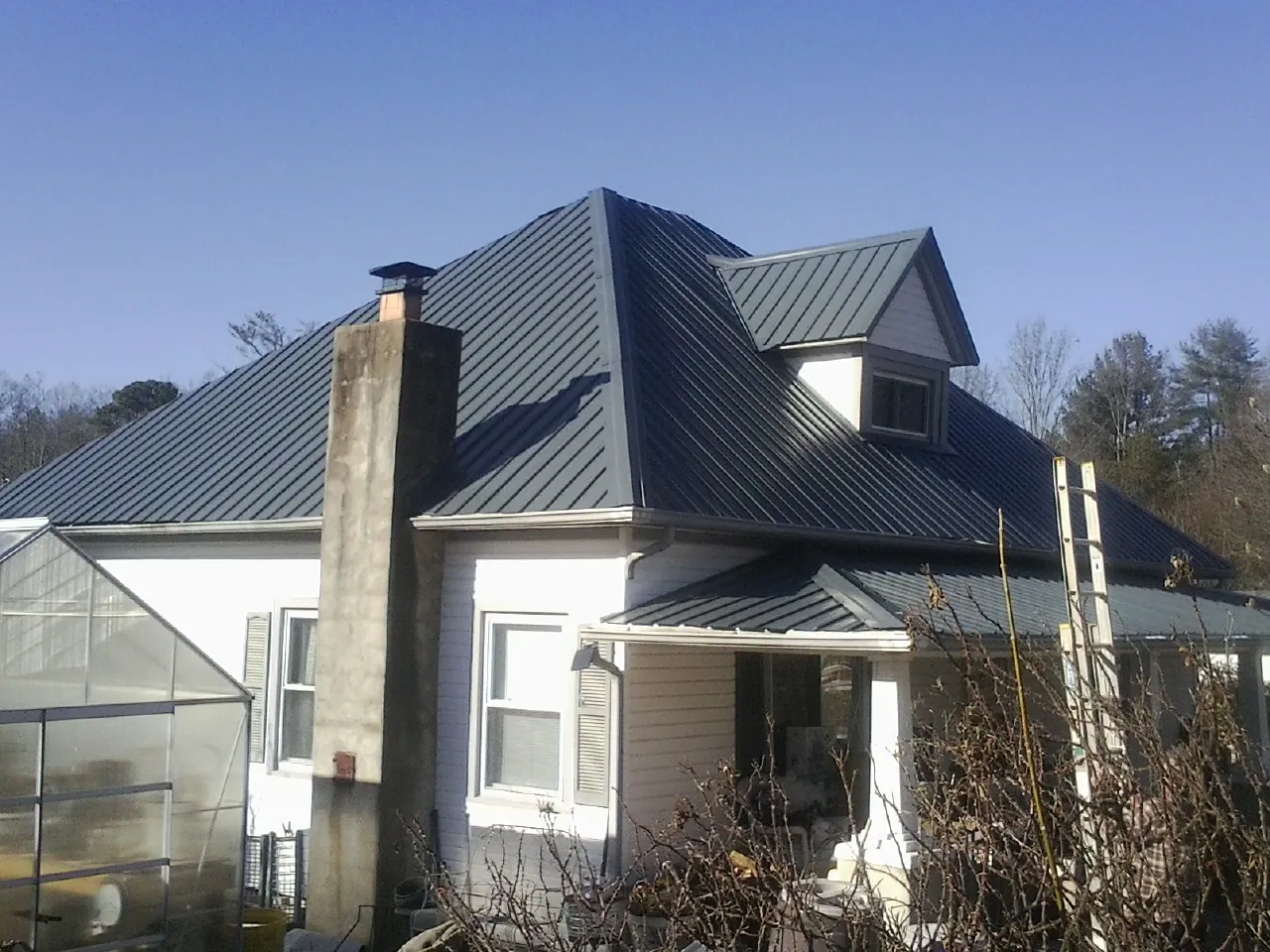 Dark blue standing seam metal roof on a white farmhouse with dormer — Slate & Tile Roof Repair by Roofing Brothers in Ether