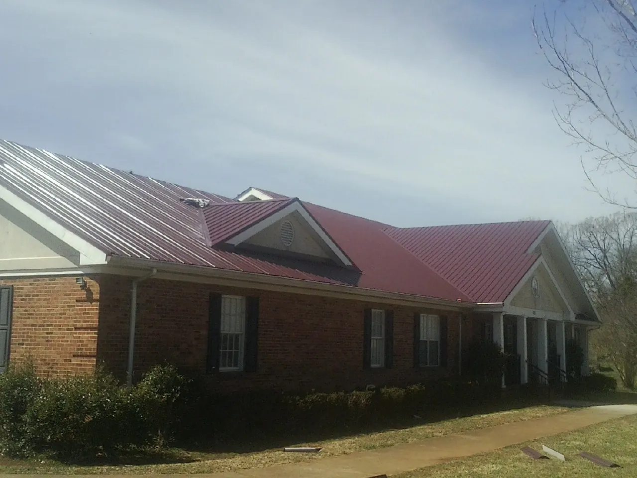 Red metal roof with gabled entries on a long brick building, from a Hail Damage Roof Repair job in Ether