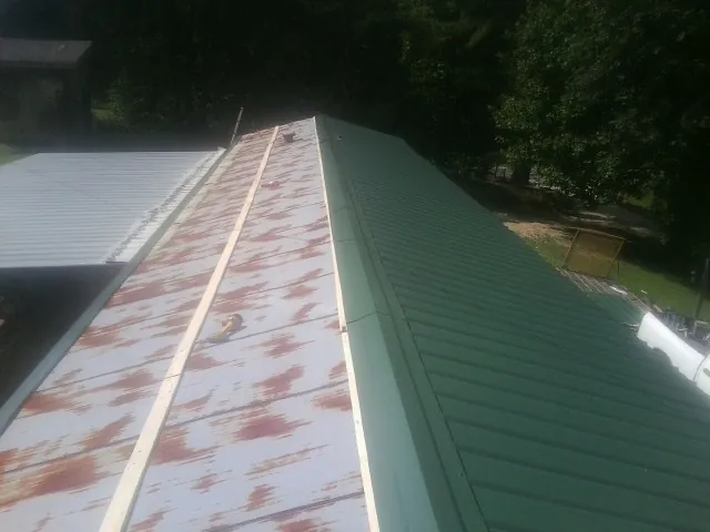 Old rusted panels beside newly installed green metal roofing — Wind Damage Roof Repair by Roofing Brothers in Ether