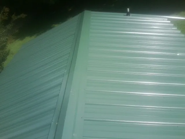 New green metal panels meeting at the ridge of a roof — Flat Roof Repair work by our crew in Ether