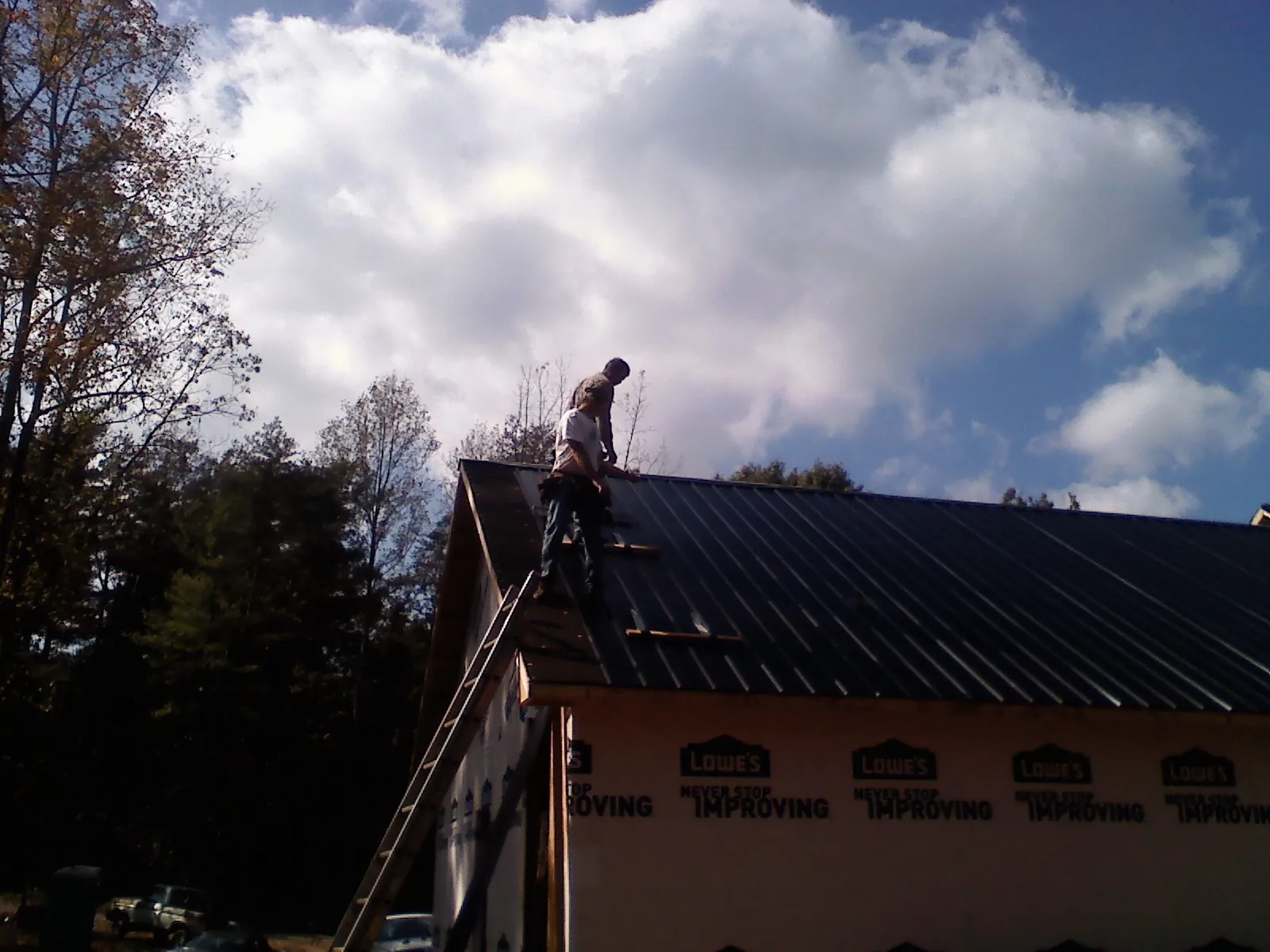 Roofer fastening dark metal panels high against a cloudy sky, from a Roof Inspection job in Ether