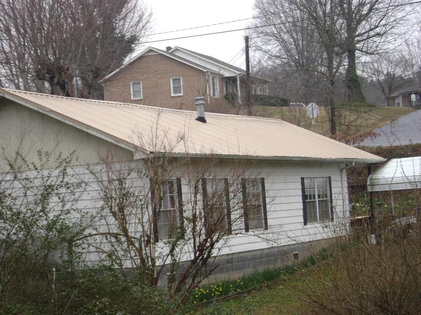 Tan metal roof on a white sided house set into a hillside — Commercial Roofing by Roofing Brothers in Ether