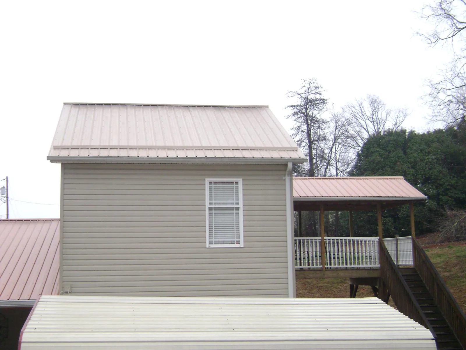 Tan metal roofs on a two story addition and attached porch, from a Roof Replacement job in Ether